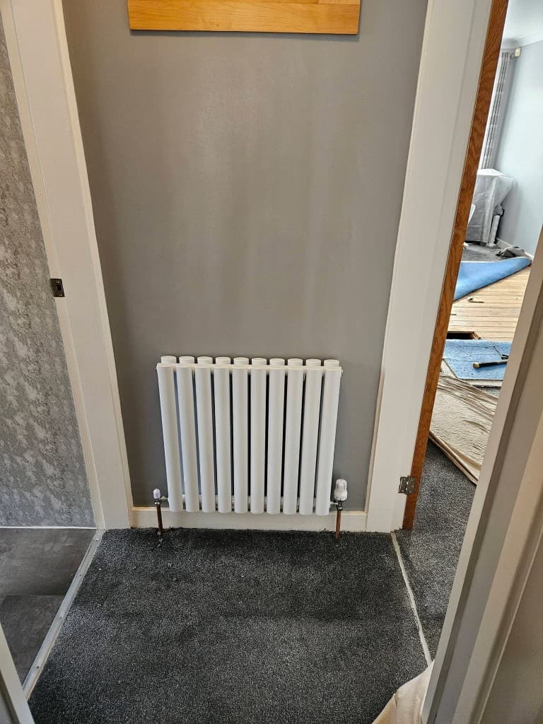 Vertical column radiator on grey wall between rooms