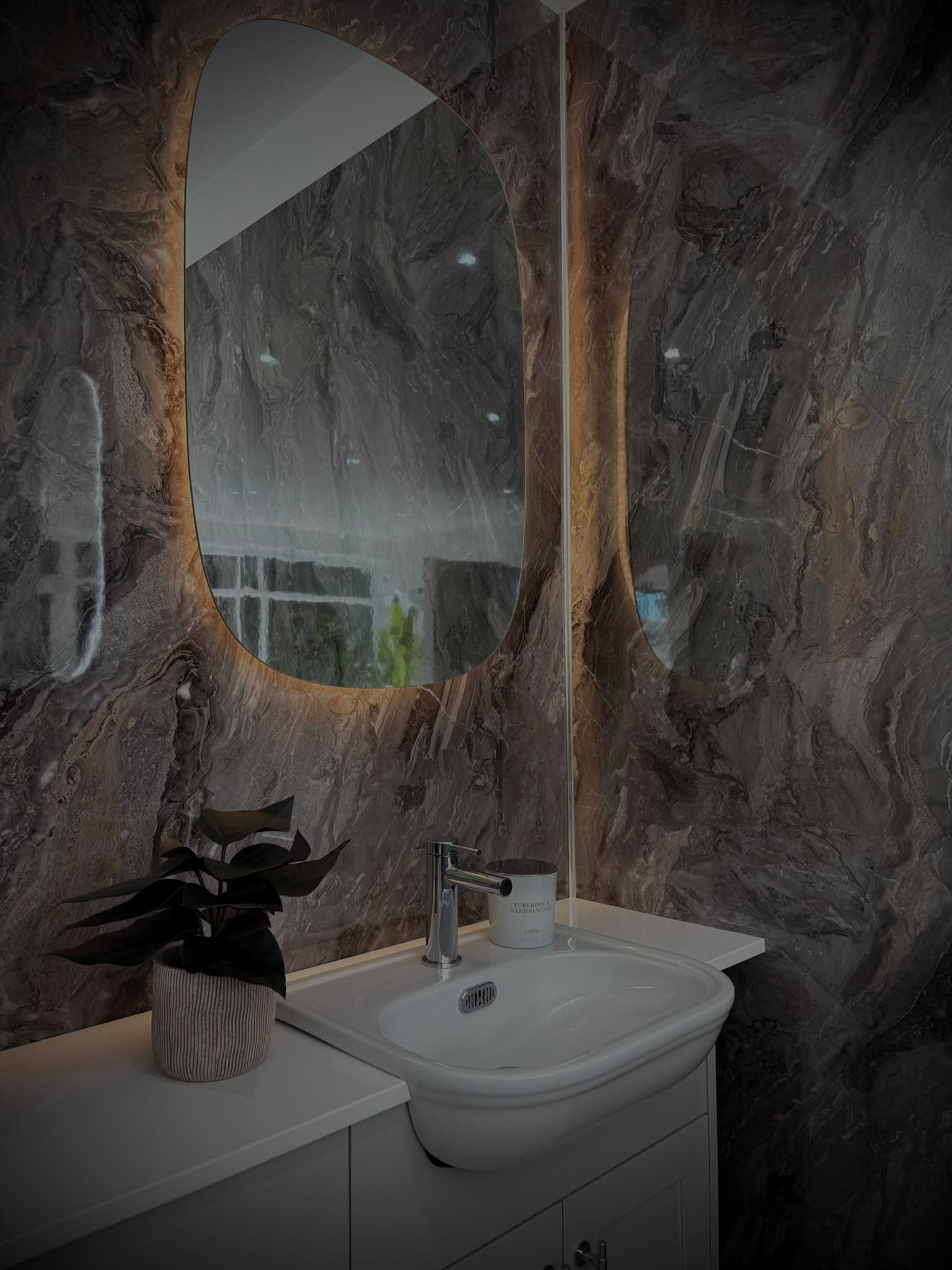 Backlit mirror on dark marble-effect wall panels above a white basin unit