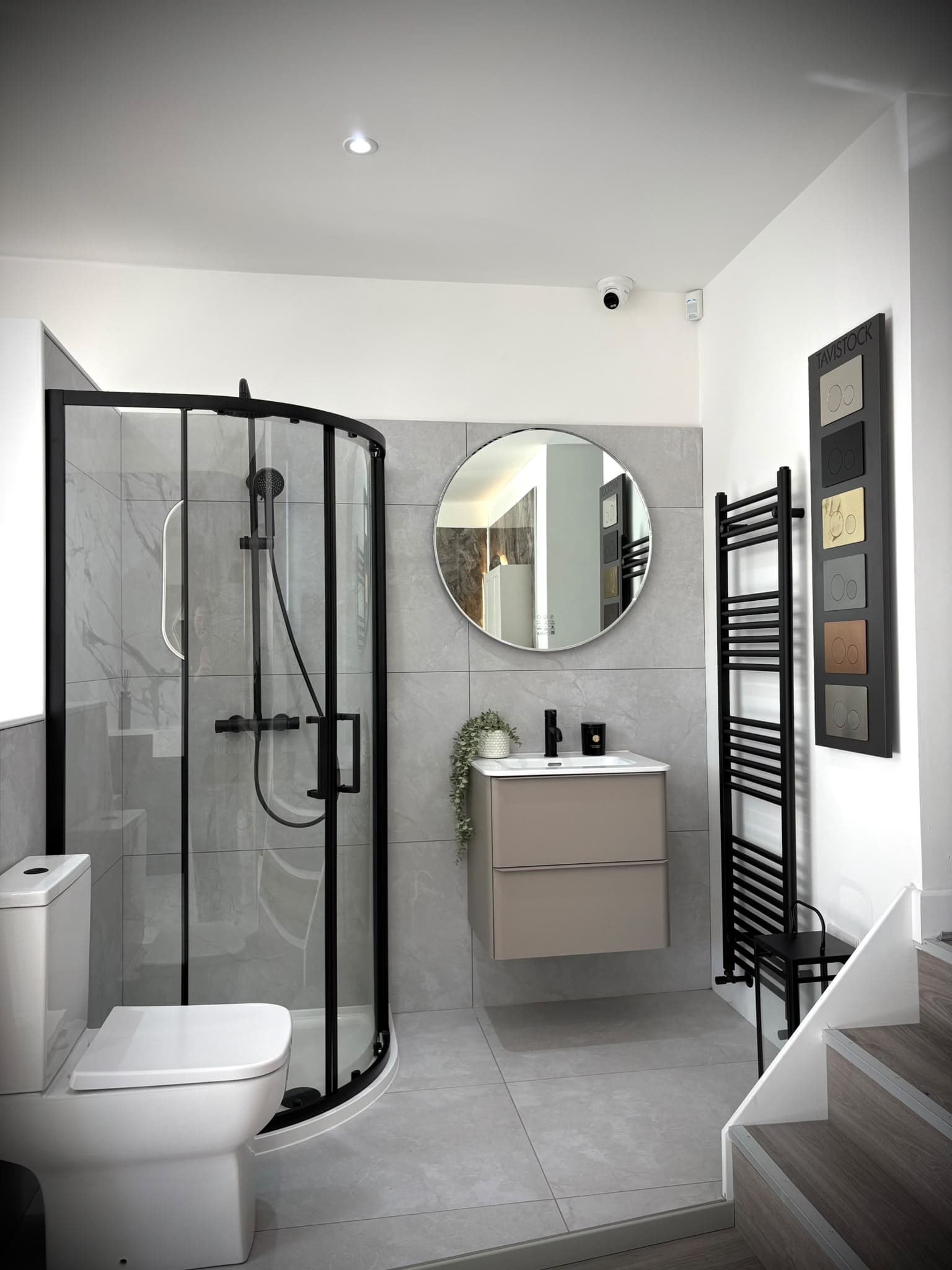 Black framed quadrant shower enclosure, taupe wall-hung vanity and round mirror in the showroom