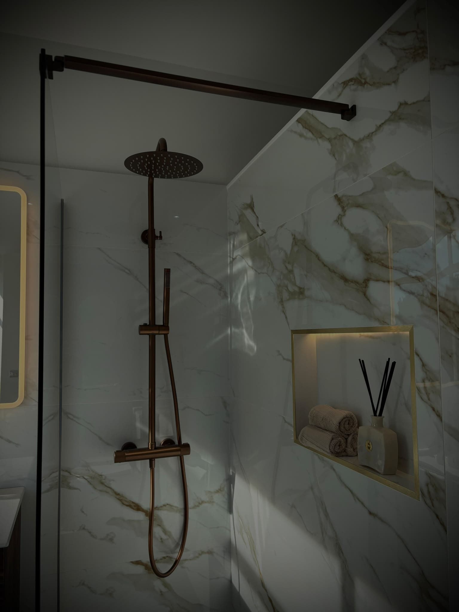Brushed copper rainfall shower in a marble walk-in shower with a lit recessed niche