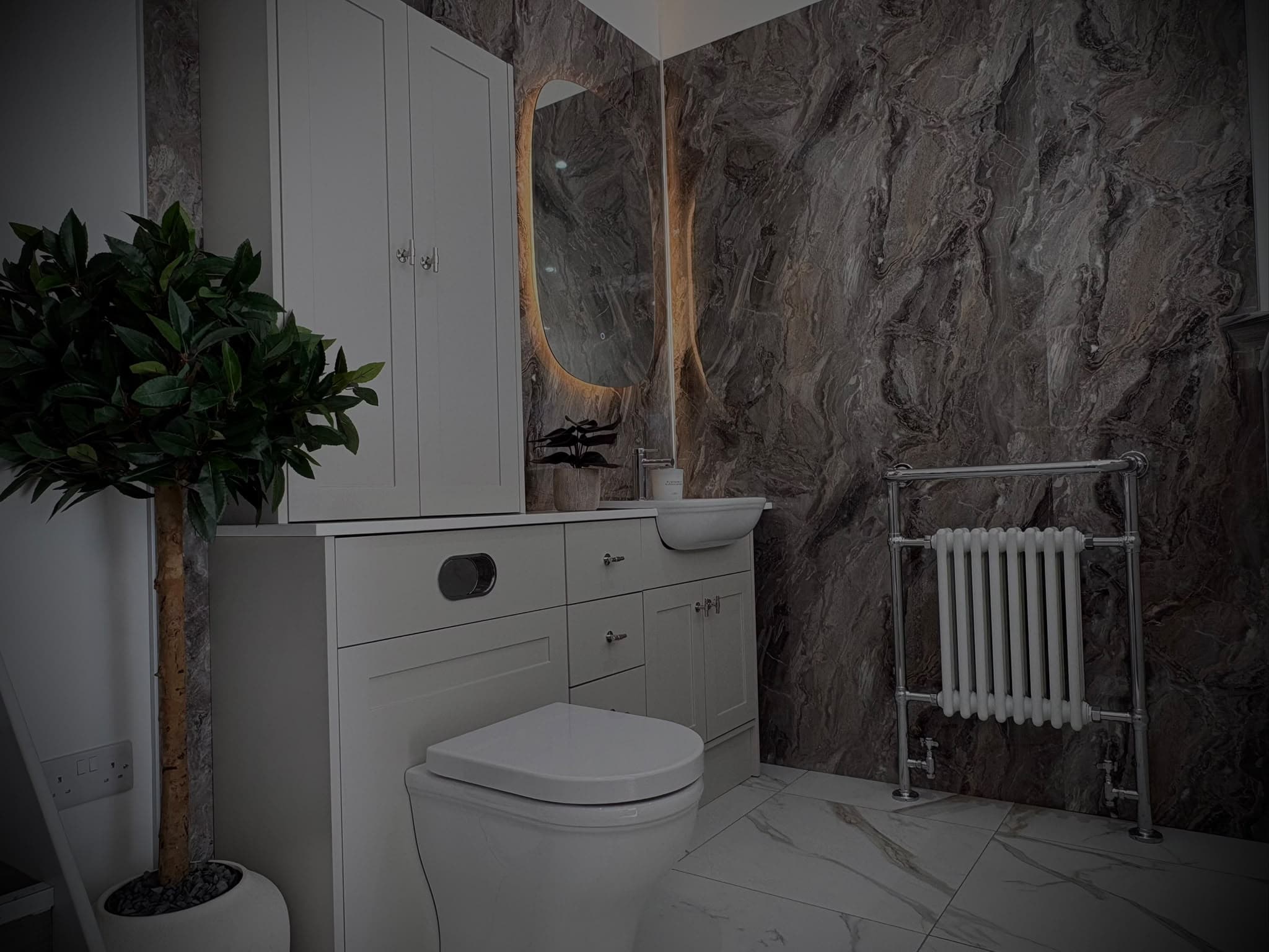 Dark marble cloakroom display with shaker vanity unit, backlit mirror and traditional towel radiator