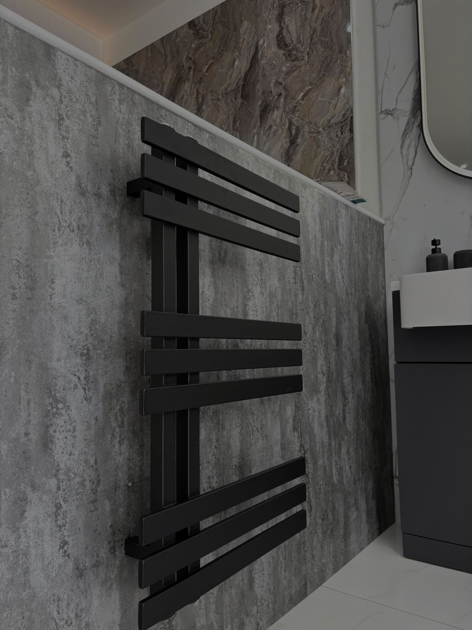 Matt black designer heated towel rail on a concrete-effect wall panel