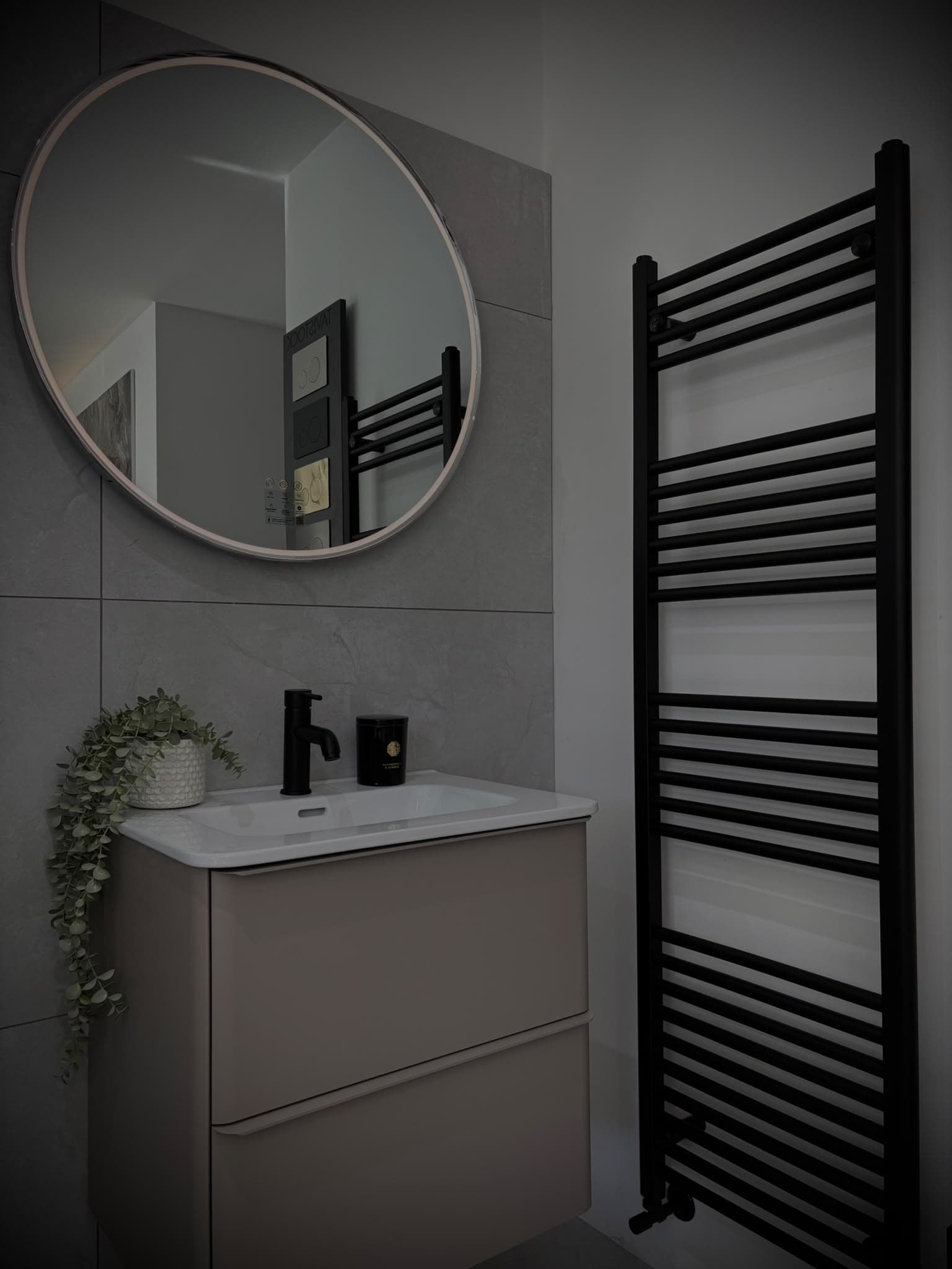 Taupe wall-hung vanity with black tap, round mirror and tall black heated towel rail