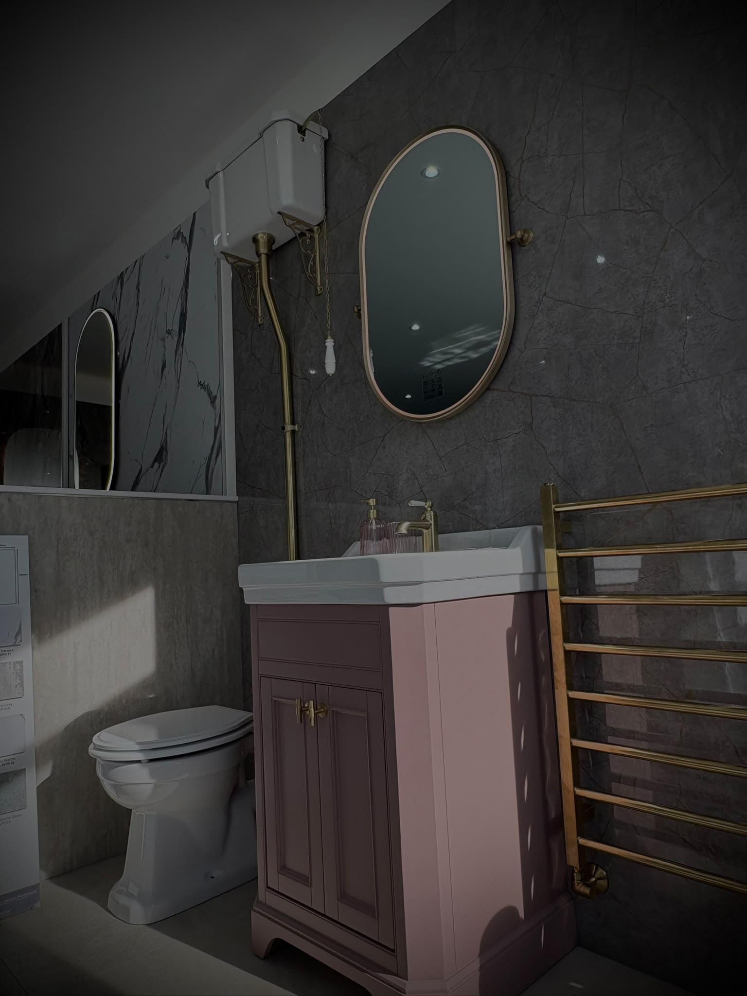 Period-style bathroom with pink vanity unit, oval brass mirror and gold heated towel rail