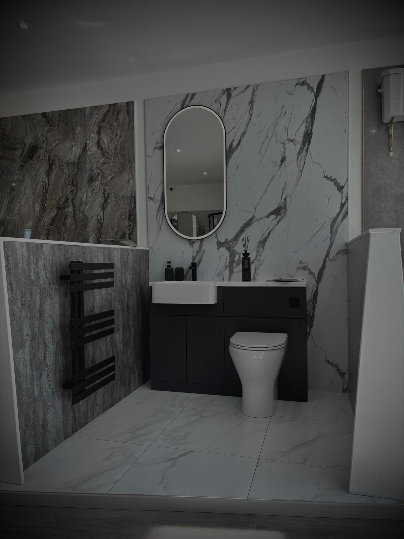 White marble bathroom display with matt black combination vanity unit and oval mirror